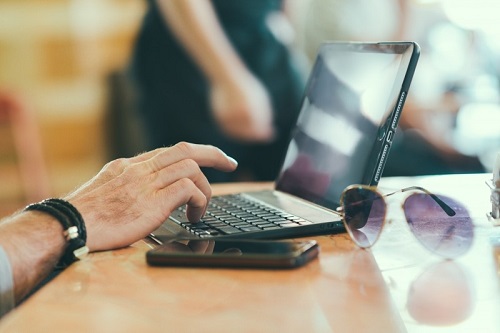 man-working-on-computer-with-mobile-phone-and-sunglasses-on-table.jpg